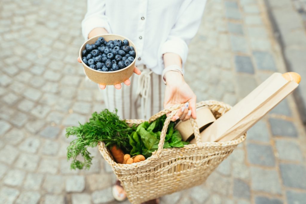 Vrouw draagt een boodschappentas vol verse groenten, bessen en andere plantaardige producten